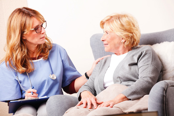 Portrait of senior woman sitting at home and consulting with middle age caregiver. Home healthcare nurse holding in her hand clipboard and giving advise while talking to elderly patinet.